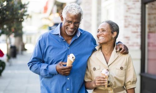 older couple walks down city sidewalk while holding ice cream cones